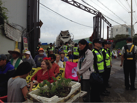 Nobel Peace laureate Mairead Maguire, Ann Wright, Catholic sisters and other Gangjeong activists after having been lifted up and carried in chairs out of the road to allow steady stream of concrete trucks to enter the naval base.