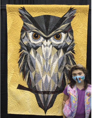 Myla, age 9, admires this owl quilt. She is a quilter too, and is  wearing a quilted vest she made herself when she was 8.